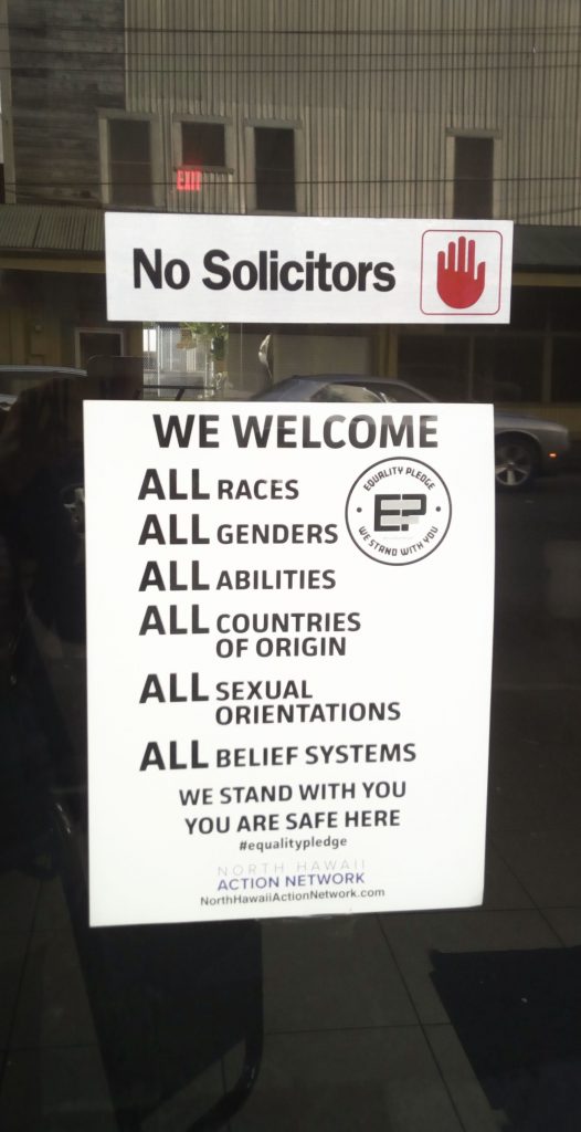 Two signs in a shopfront in Downtown Hilo, one welcoming everyone, the other one excluding solicitors.